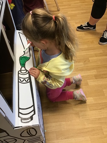 A child kneeling in front of a cardboard bus while colouring it