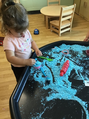 A child scooping moon sand into a cupcake liner at a sensory tray