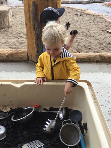 A child scooping soil in a sensory bin outside