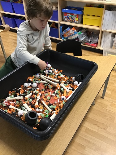A child playing in a sensory bin filled with Halloween themed items