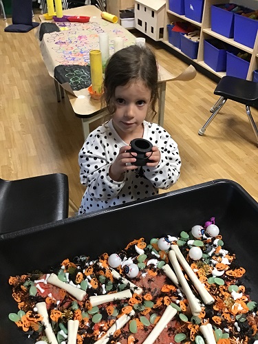 A child playing in a sensory bin filled with Halloween themed items