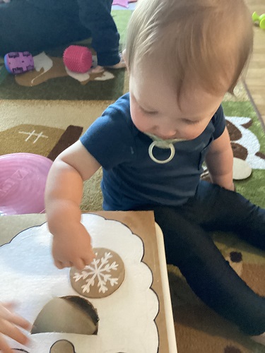 An infant feeding a cardboard Santa a snowflake