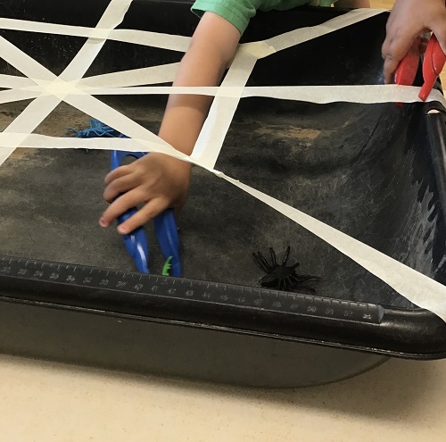 A child's name using tongs to remove a toy bug from a tape web