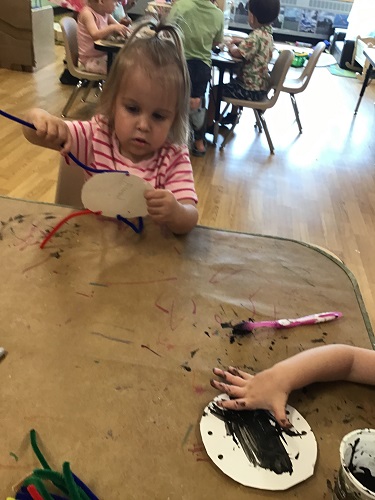 Two children at a table painting on a paper plate