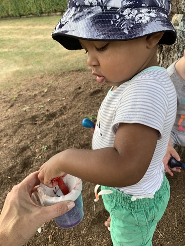 A child dipping a paint brush into a paint pot 