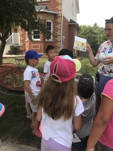 A groupd of children and an educator looking at a page of a story outside