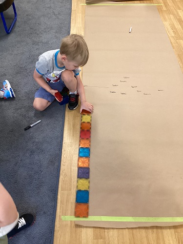 A child adding magnet tiles to the long line of tiles on the floor