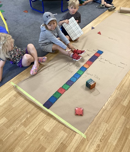 Children sitting next to a large brown paper with magnet tiles lined up the length of the paper