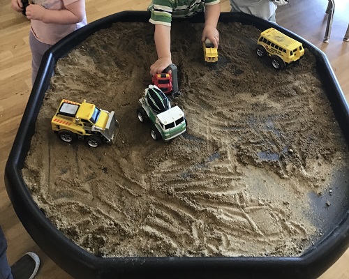 Children driving cars and trucks in the sand 
