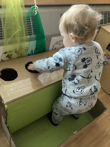 An infant standing inside a cardboard ball drop