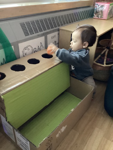 An infant squatting beside a cardboard ball drop