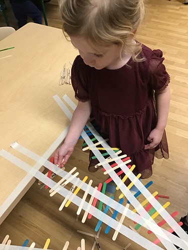 A child sticking popsicle sticks to tape to create a bridge