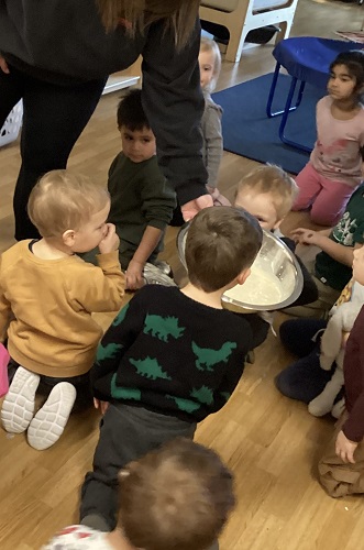 An educator holding a bowl in front of the children filled with ingredients to make ice cream