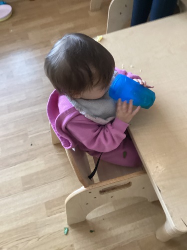 An infant sitting at a table drinking green juice out of a cup