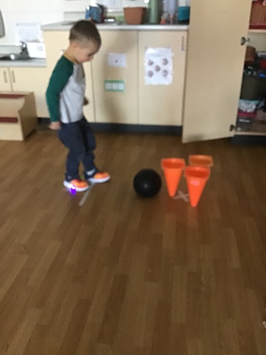 A child kicking a ball into cones set up like bowling pins