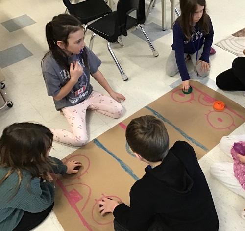 Children sitting on the floor around a large paper coloured to represent a hockey rink