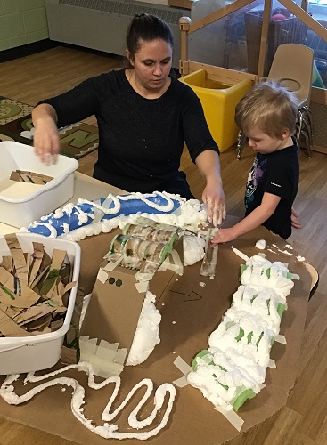 An educator and child putting paper mache on the track they created