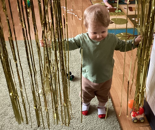 A child walking through the tinsel with his arms spread open