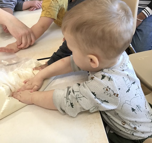 Children at a table helping to squish the dough in a ziploc bag