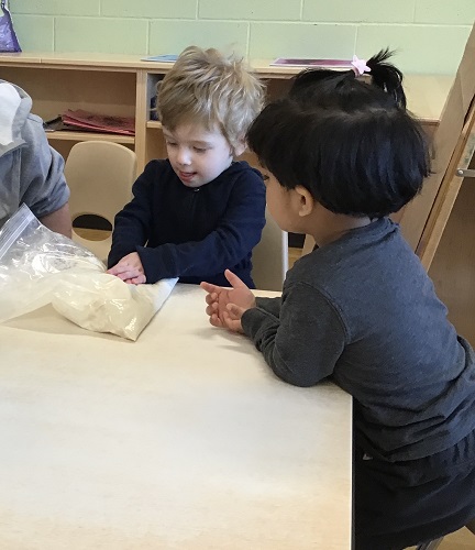 Children at a table helping to squish the dough in a ziploc bag