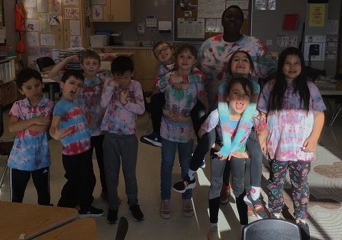 A group of children and an educator showing off their tie dye shirts
