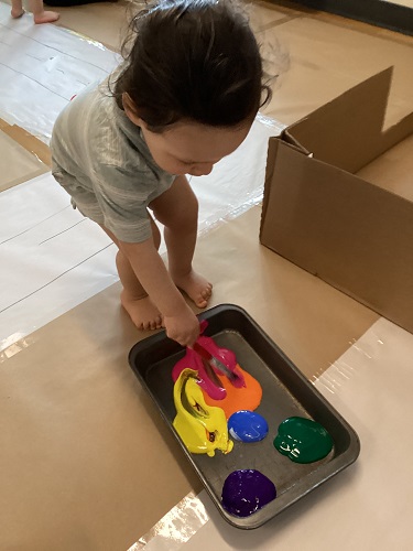 A child bending forward to dip his paint brush into the paint