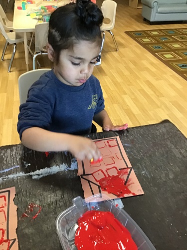 A child painting a house with red paint