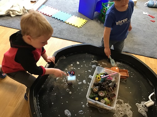 Children using brushes to wash the mud off the toy cars and trucks at the Tuff Tray