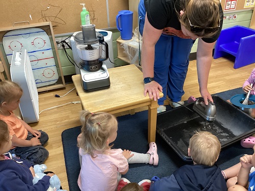 An educator using a hand mixer to make bubbles while the children watch