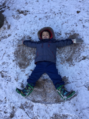 School age 1 child laying in the snow making a snow angel 