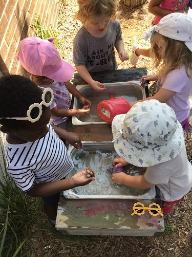 5 Preschool children standing around the sensory bin with water and watering can