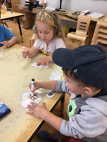 3 Preschool children sitting at the table with their slime colouring the slime with markers