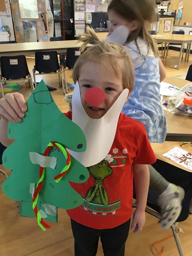 School age 1 child with a santa beard, red nose and holding a christmas tree