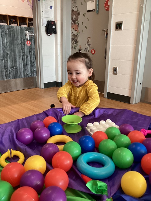 An infant child playing at a tuff tray with various colourful objects