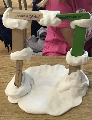 child sitting in the background of a tower built out of Jenga blocks and clay