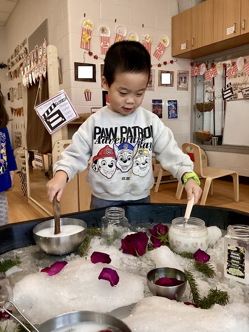 A preschool child scooping snow from 2 bowls