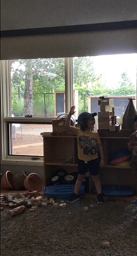 A preschooler is standing in front of a space ship he built out of blocks.