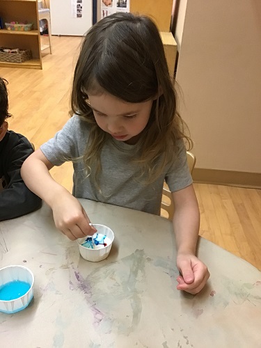 A preschooler is using a small dropper to add blue food colouring to milk.