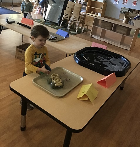 A preschooler is using a spray bottle to spray a vehicle to wash.