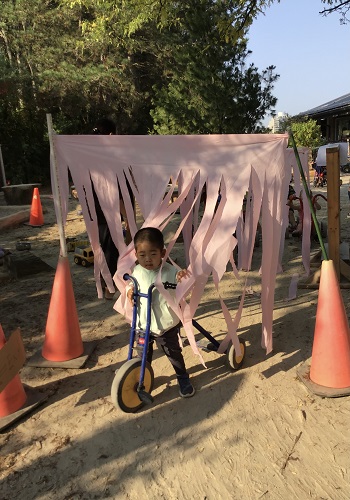 A preschooler is riding their bike through a piece of fabric that is part of their car wash.