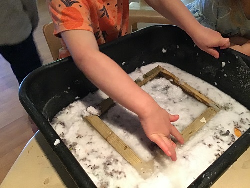 A preschooler is pressing a screen frame into a bucket with lavender pulp.