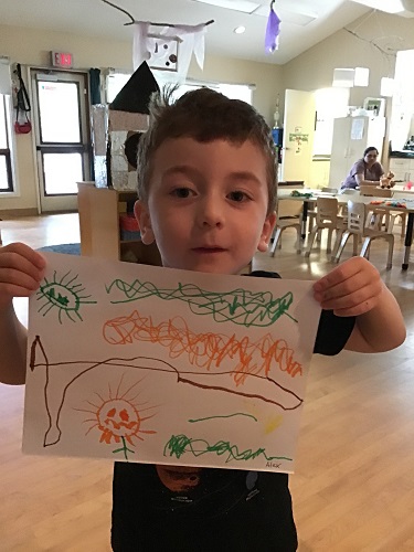 A preschooler holds up a picture of the sunflowers that they drew.