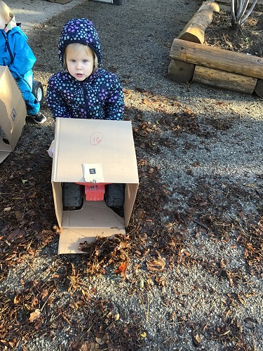 A toddler is riding on a car with a box on the front.