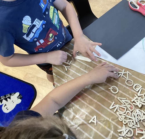 2 School Age 1 children, one child organizing letters in order, another child collecting letters