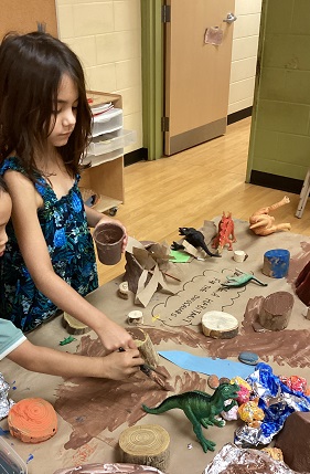 Child creating a prehistoric scene with tin foil and materials 