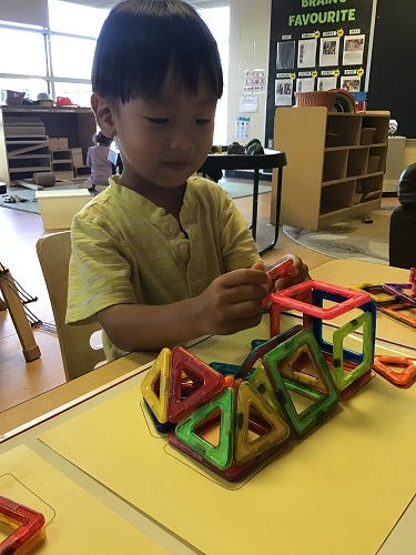 preschool boy building dinosaur out of megnatiles 