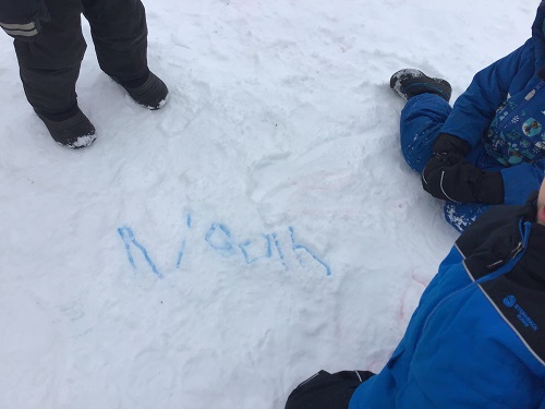 Child writing name in snow with markers