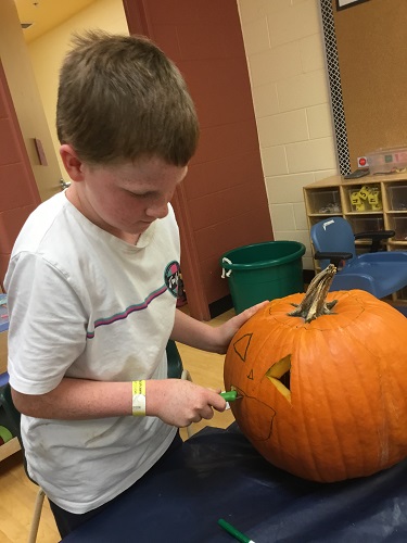 school-age boy carving eye out of pumpkin 