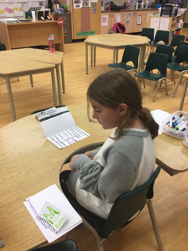 school-age girl sitting at table with handmade register for store 