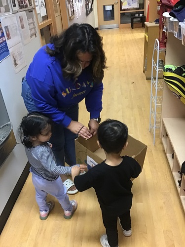 Educator and children carrying box down hall for shoe drive 